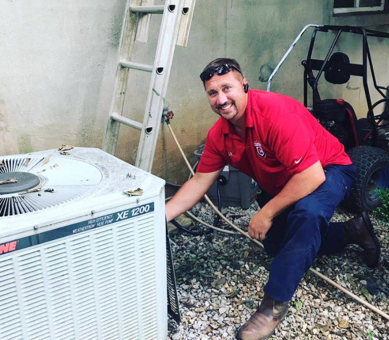 A Comfort HVAC tech working on a broken AC unit while smiling.